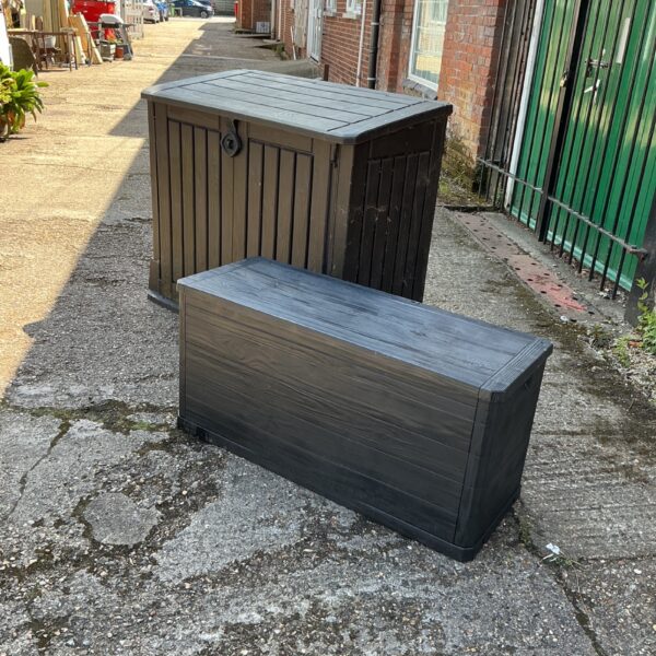 Dark grey plastic garden storage box in a yard.