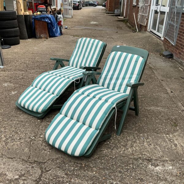 Two green plastic sunloungers with striped cushions in a garden setting.