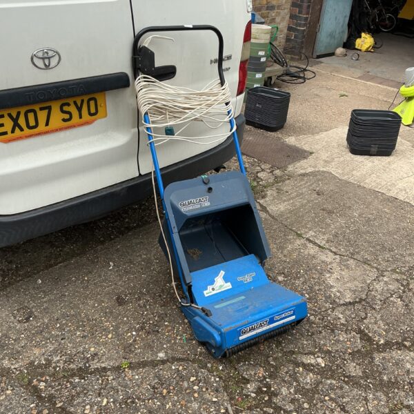 Vintage Qualcast RE35 lawn raker in a garden setting.