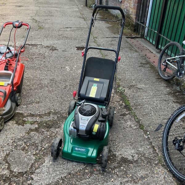 Side view of a vintage Qualcast petrol lawnmower in a garden.