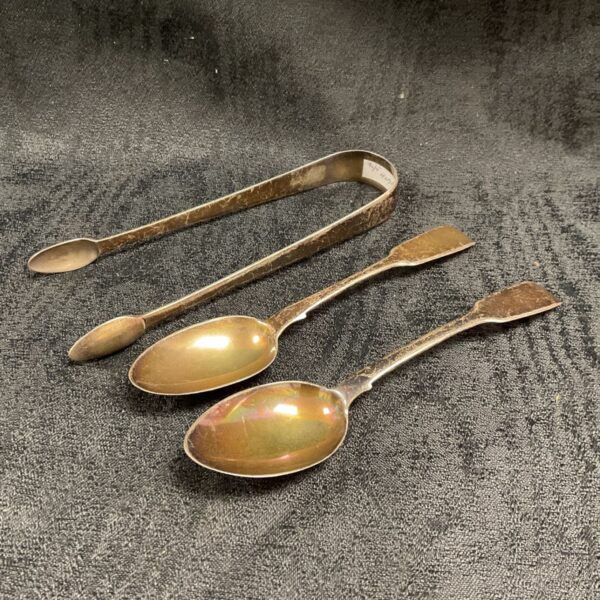 Antique silver Georgian teaspoons and tongs on grey background.