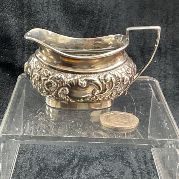 Antique silver repousse cream jug with floral design.