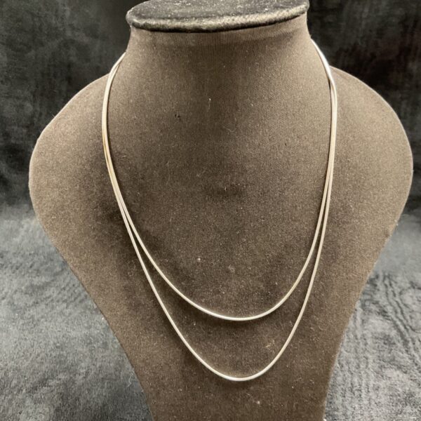Layered silver snakelink necklaces on display, delicate jewelry.