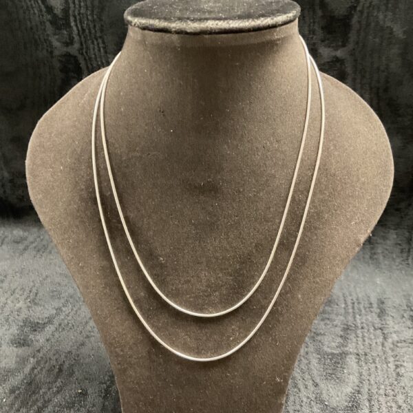 Layered silver snake chain necklaces on display.
