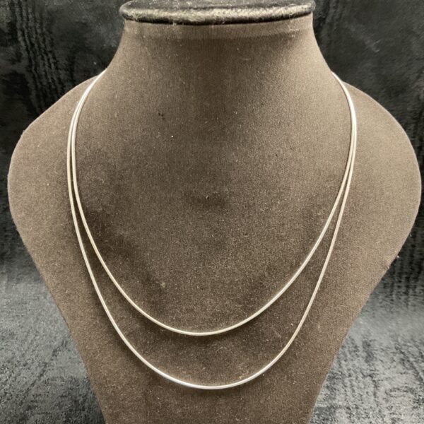 Pair of delicate silver snake chain necklaces on a display.