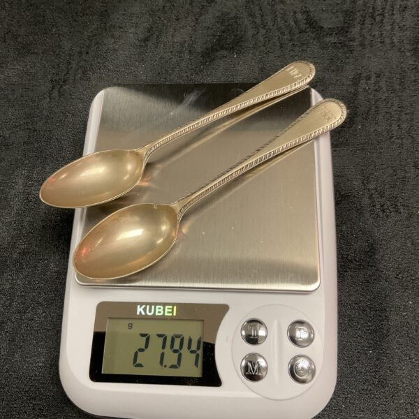 Silver teaspoons on a digital scale showing 27.9g weight.