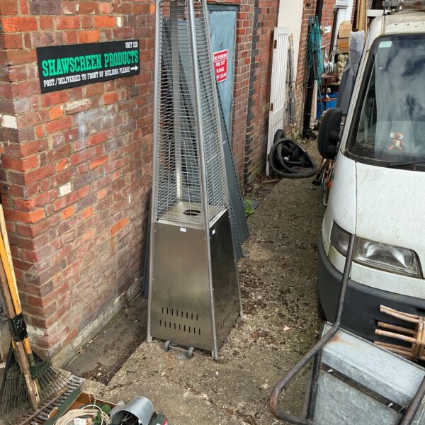 Tall stainless steel patio gas heater in a garden setting.