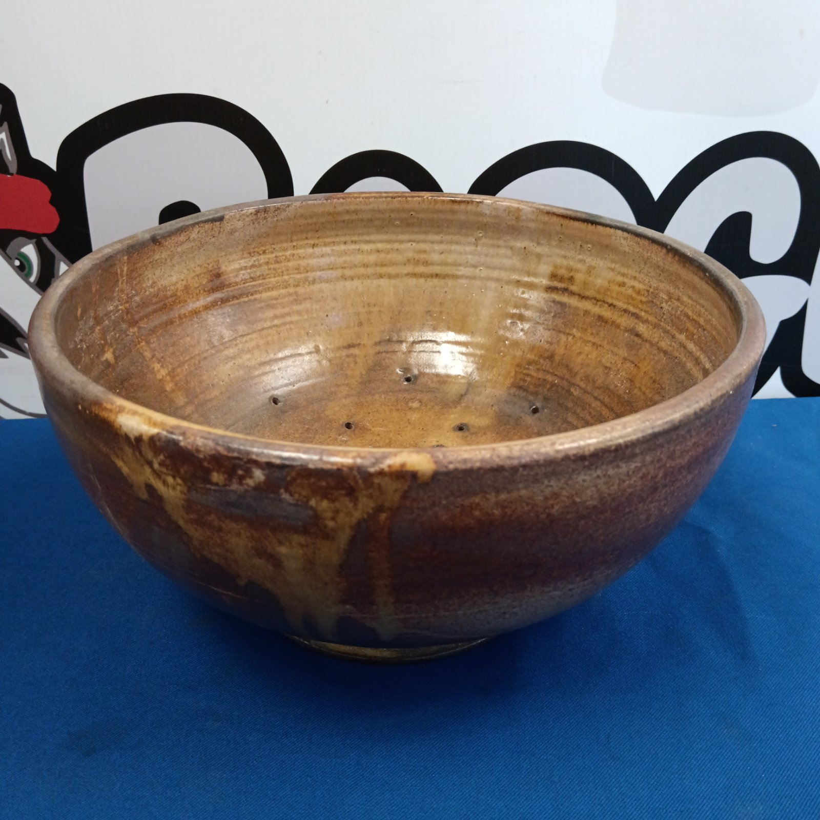 Large studio pottery bowl with brown glaze on a blue surface.