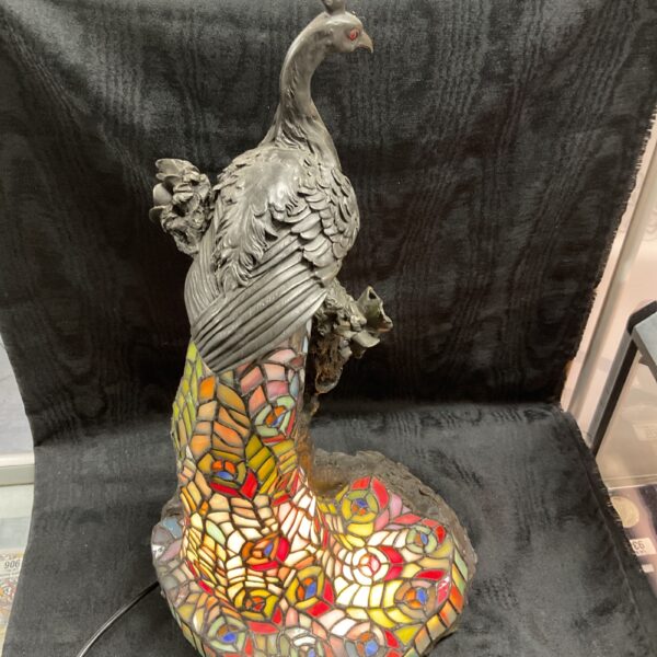 Detailed side view of a vintage Tiffany style peacock lamp.