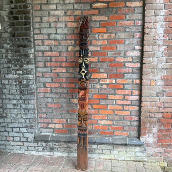 Large carved tribal totem pole against brick wall.