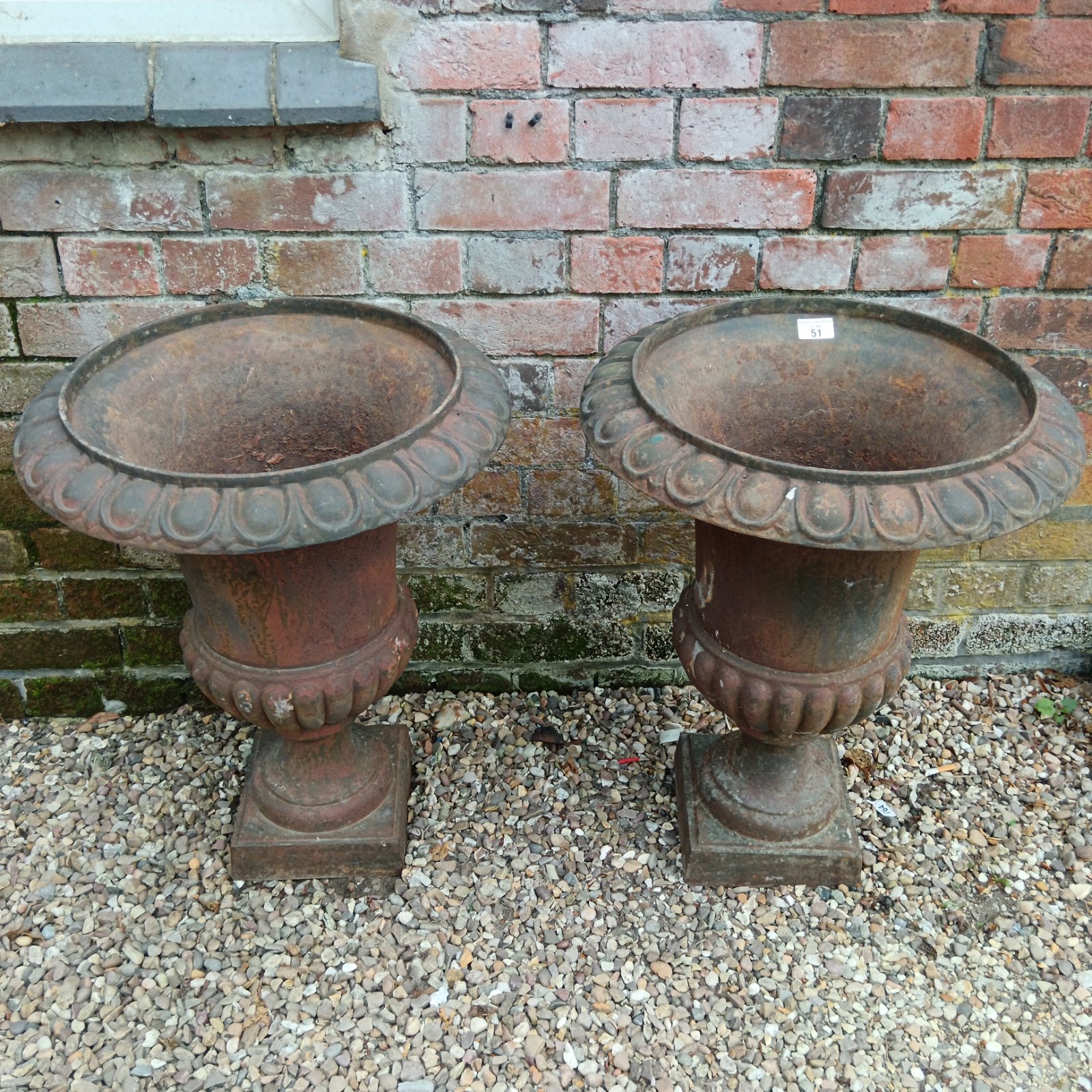 Pair of weathered Victorian cast iron urn planters in a garden.