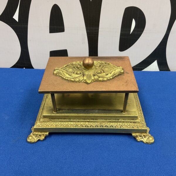 Vintage brass and copper matchbox holder on a dark surface.