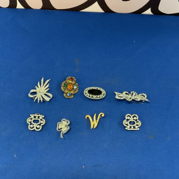 Close-up of a vintage brooch lot with colourful enamel details.