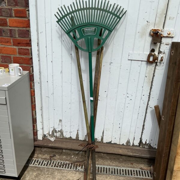 Vintage metal garden rake with green head and wooden handle.