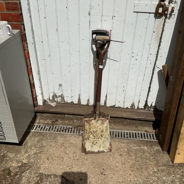 Weathered vintage garden shovel leaning against a wall.