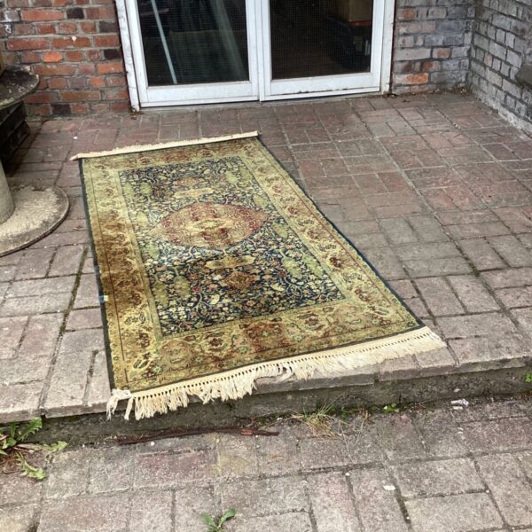 Vintage green and brown rug displayed outdoors.