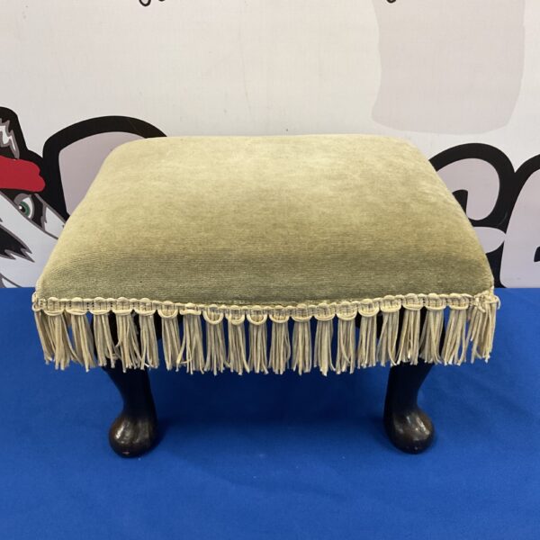 Vintage green footstool with decorative tassels and turned legs.