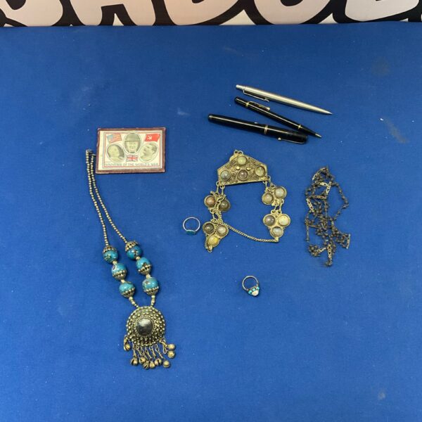 Vintage jewellery lot with colourful necklaces, silver rings, and pens.