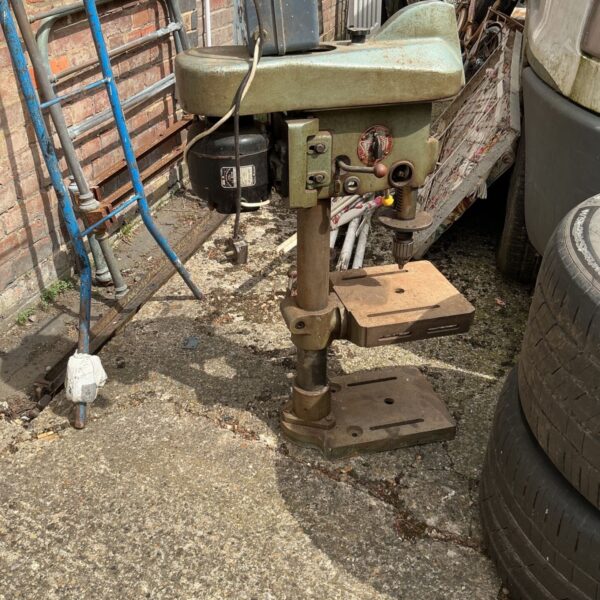 Vintage industrial pillar drill in a workshop setting.