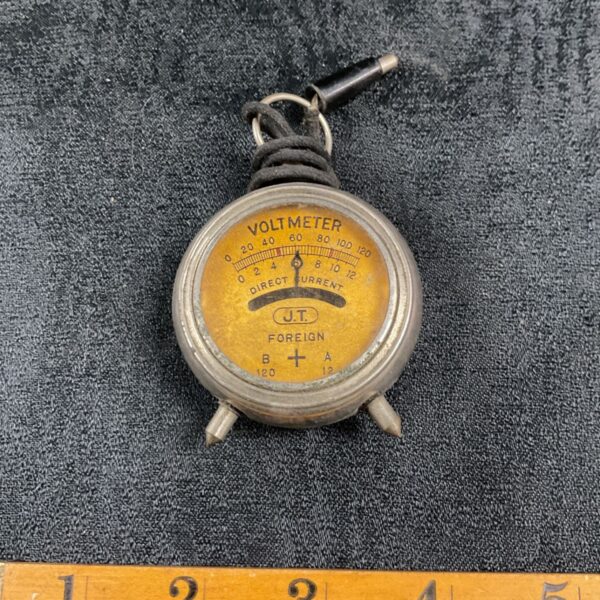 Vintage pocket voltmeter with a circular dial and chain attachment.