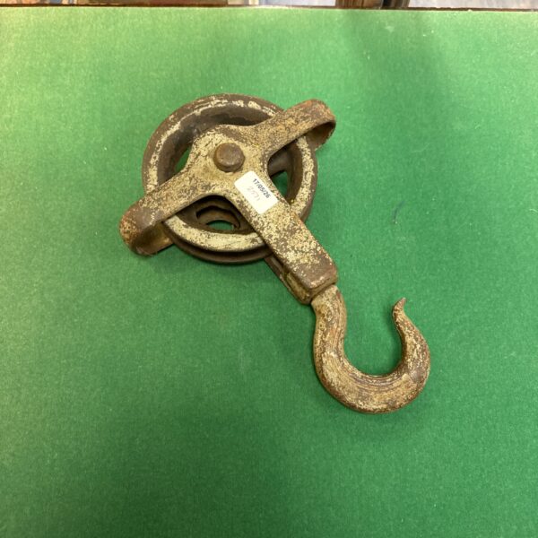Vintage pulley hook with weathered metal and a sturdy wheel.