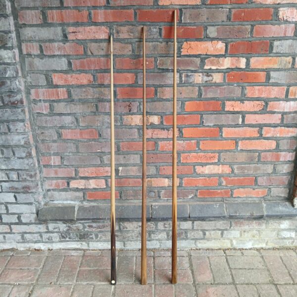 Lot of three vintage snooker cues against a brick wall.