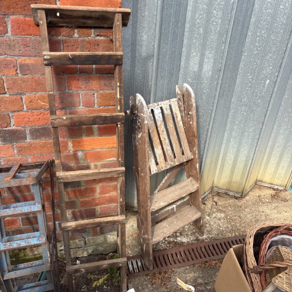 Two weathered vintage wooden ladders in a garden setting.