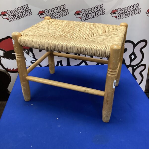 Vintage woven footstool with wooden legs, rustic farmhouse style.