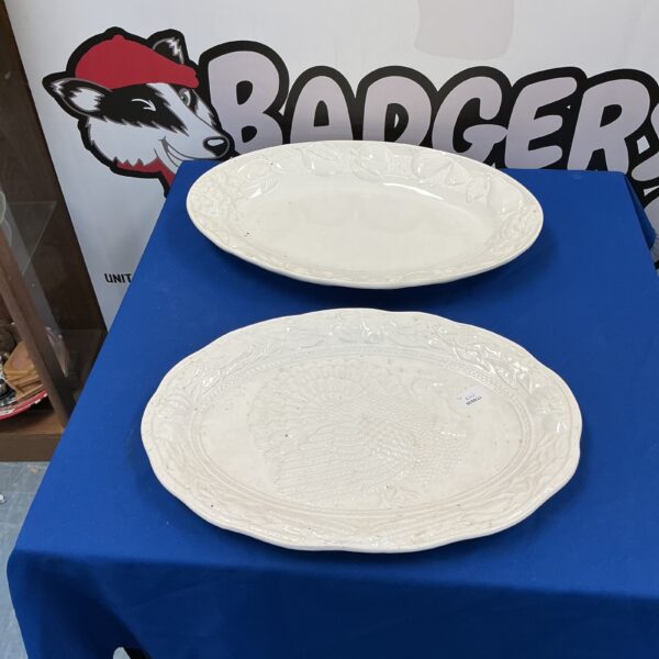 Two large white porcelain meat plates on a blue surface.