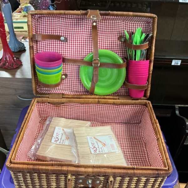 Vintage wicker picnic basket filled with colourful picnic set.