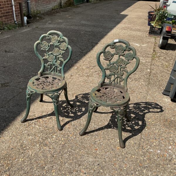 Antique wrought iron garden chairs with floral detailing in a garden setting.