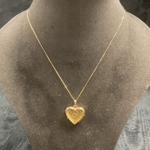 Close-up of 9ct gold heart locket necklace on display stand.