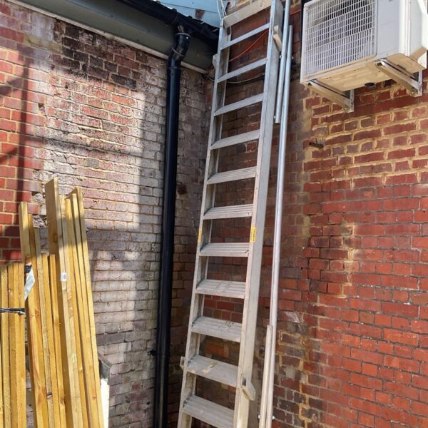 Large aluminium mezzanine access ladder leaning against brick wall.