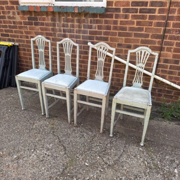 Four antique distressed dining chairs in a garden setting.