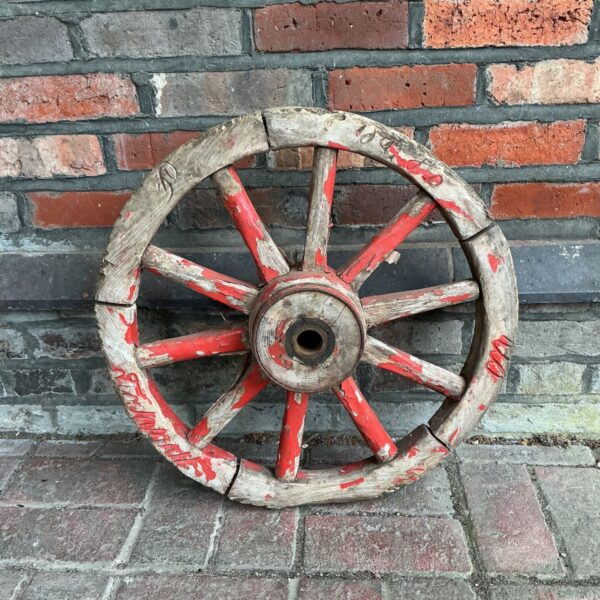 Antique wooden cart wheel with red paint and weathered spokes.