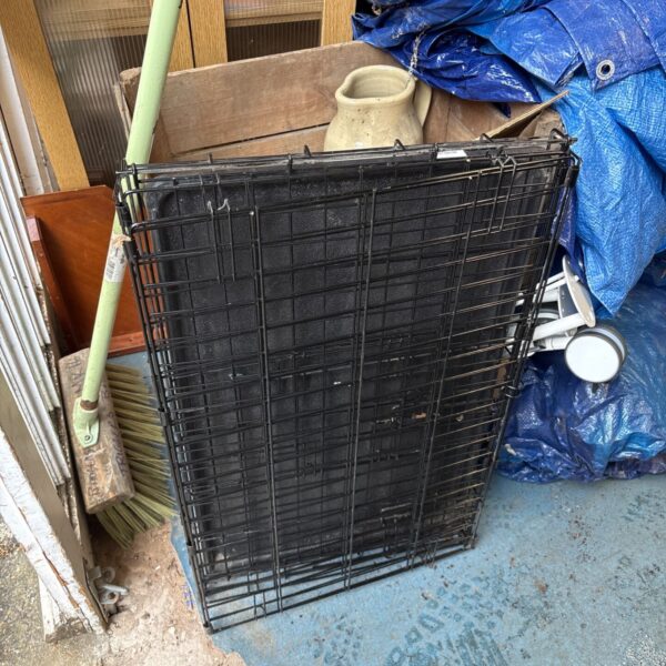 Black folding dog crate with blue tarp in background.