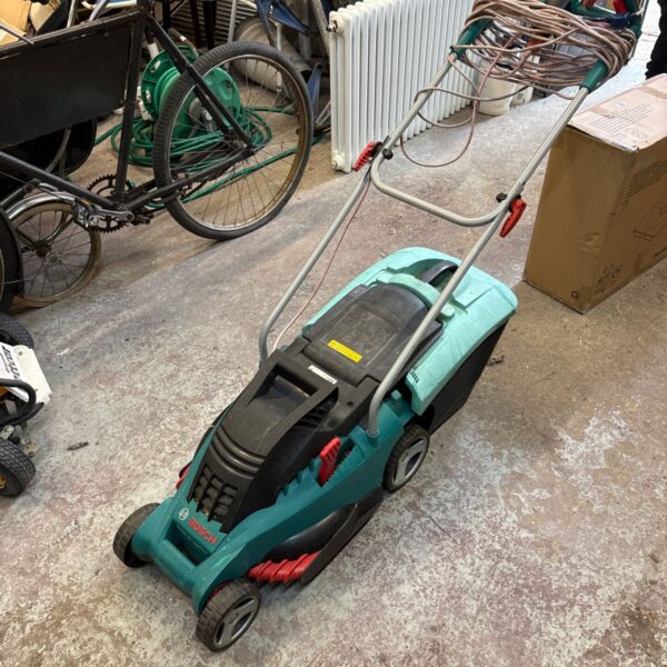 Green Bosch electric lawn mower in a workshop setting.