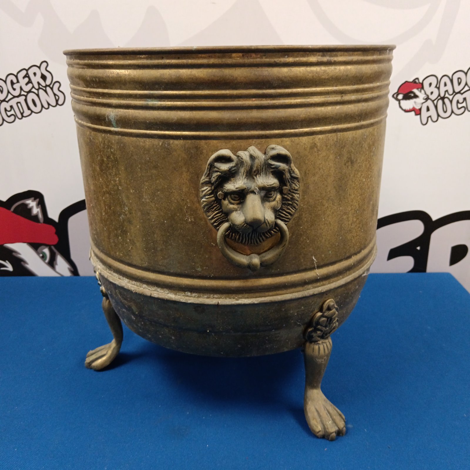 Antique brass log bin with lion head handles and claw feet.