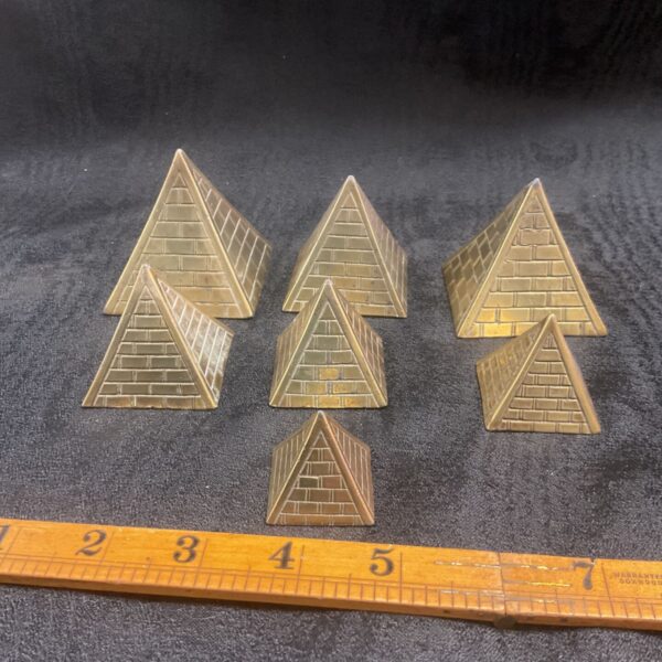 Graduated set of four brass pyramid paperweights on dark surface.