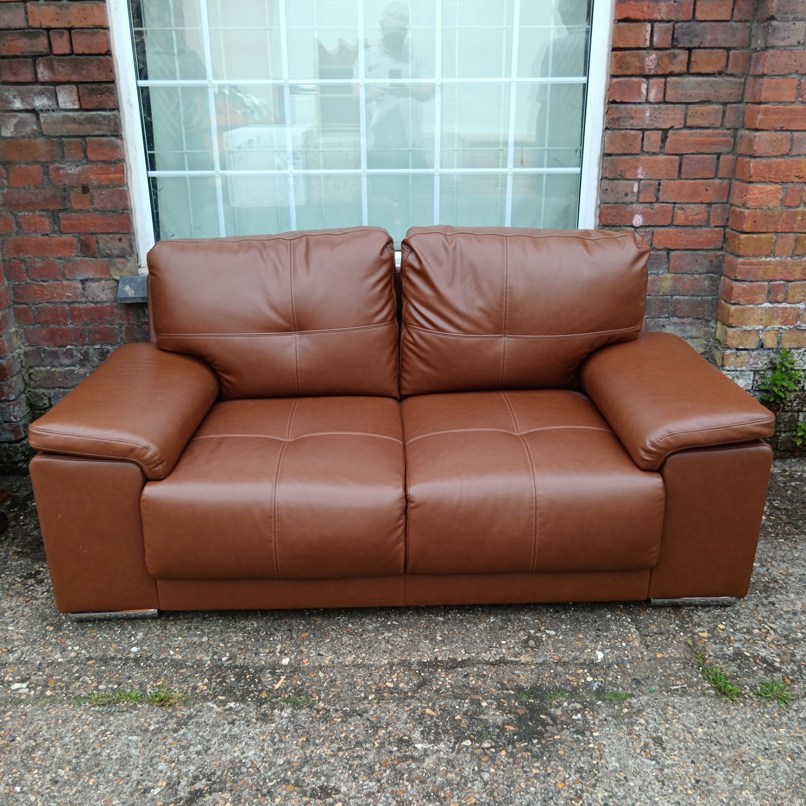 Brown leather two-seater sofa in a home setting.