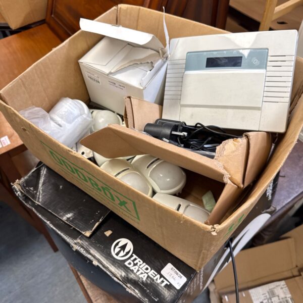 Open cardboard box containing a vintage burglar alarm system and sensors.