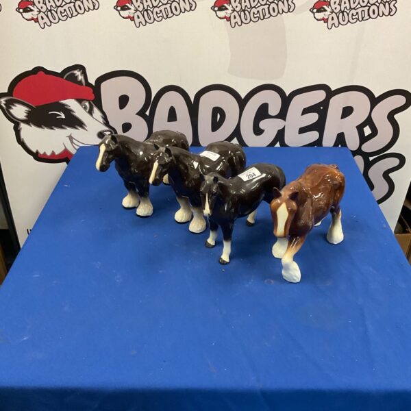 Four ceramic shire horse figures on a dark surface.