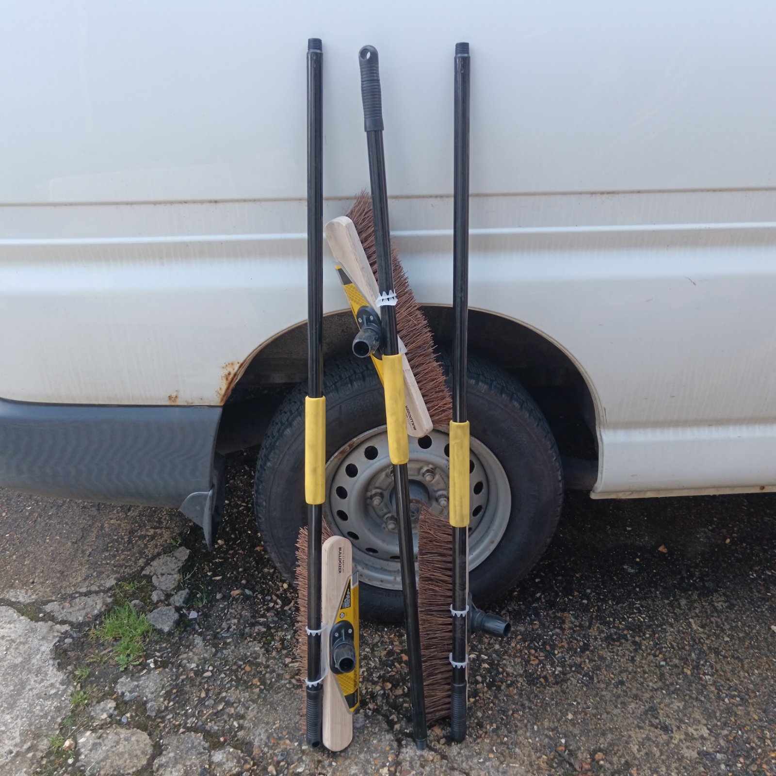 Three Charles Bentley bulldozer brooms leaning against a van tyre.