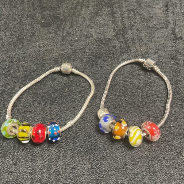 Two silver-tone charm bracelets with colourful charms displayed.
