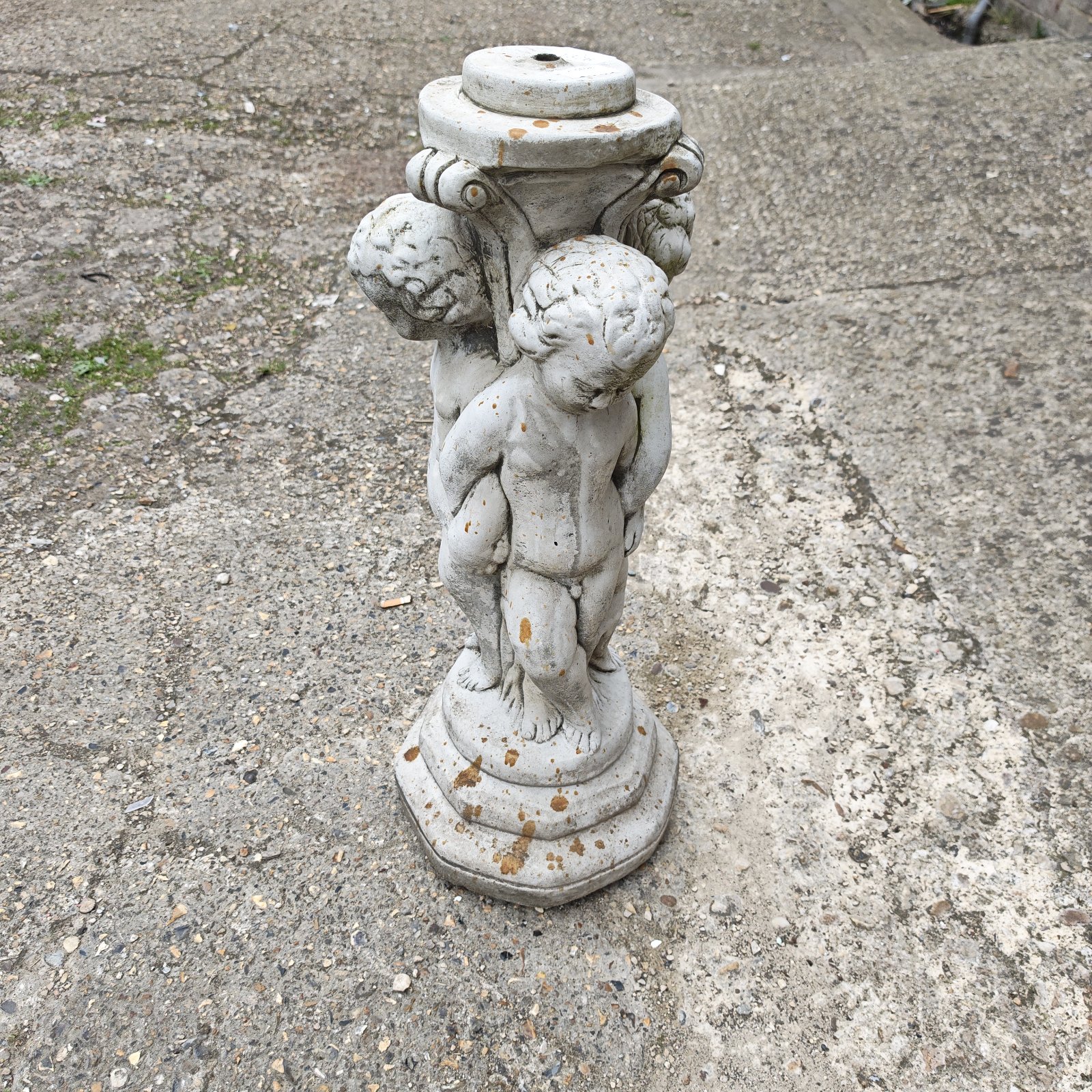 Stone cherub bird bath base in a garden setting.
