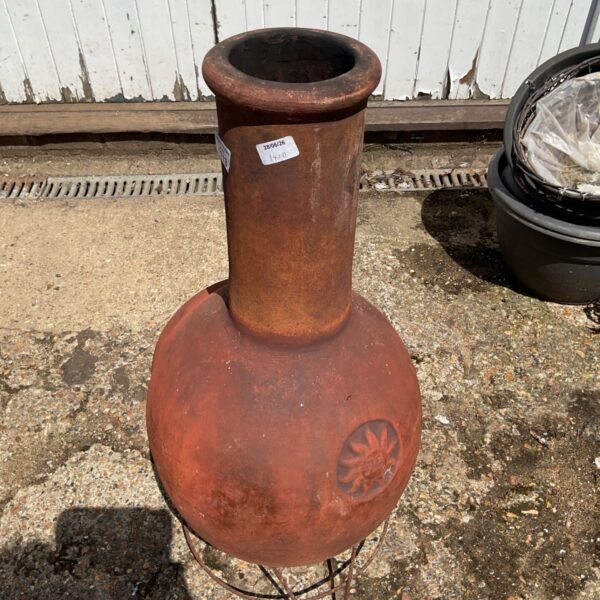 Terracotta clay chimenea with a steel stand in a garden setting.