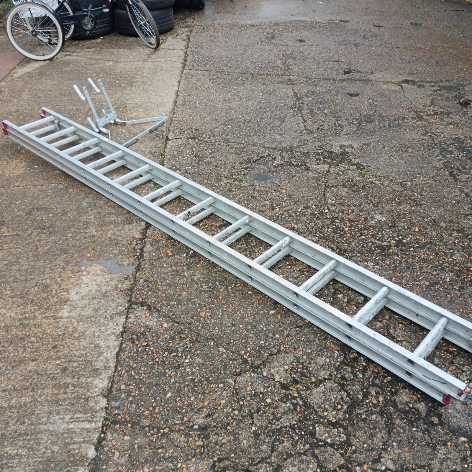 Large aluminium extending ladder with ladder stay on a paved surface.
