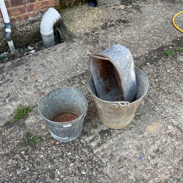 Vintage galvanised buckets and metal planter in a garden setting.