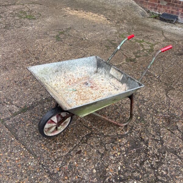 Vintage galvanised wheelbarrow in a garden setting.