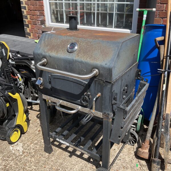 Metal garden BBQ with integrated pizza oven, showing signs of weathering.